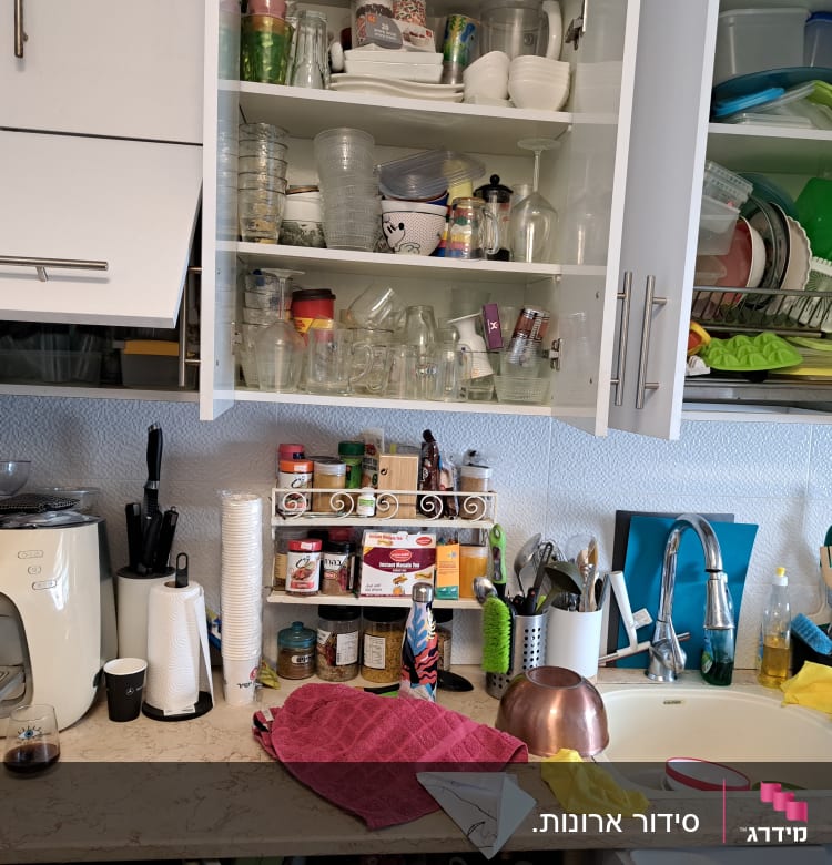 מטבח עם ארונות פתוחים, כלים, תבלינים ומוצרי ניקוי על השיש